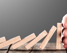 risk mitigation as demonstrated by a hand stopping falling dominoes