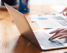 Person working on laptop while marking paper with graphs