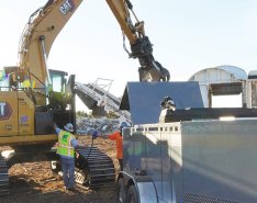 Worker in vest and hard hat with hand on heavy equipment