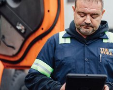 Man in work clothes standing in front of bright orange vehicle