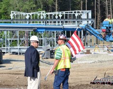 Two men are on a construction site, talking in front of a piece of machinery