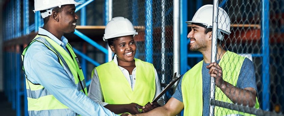 Workers in green vests and hard hats smiling and shaking hands